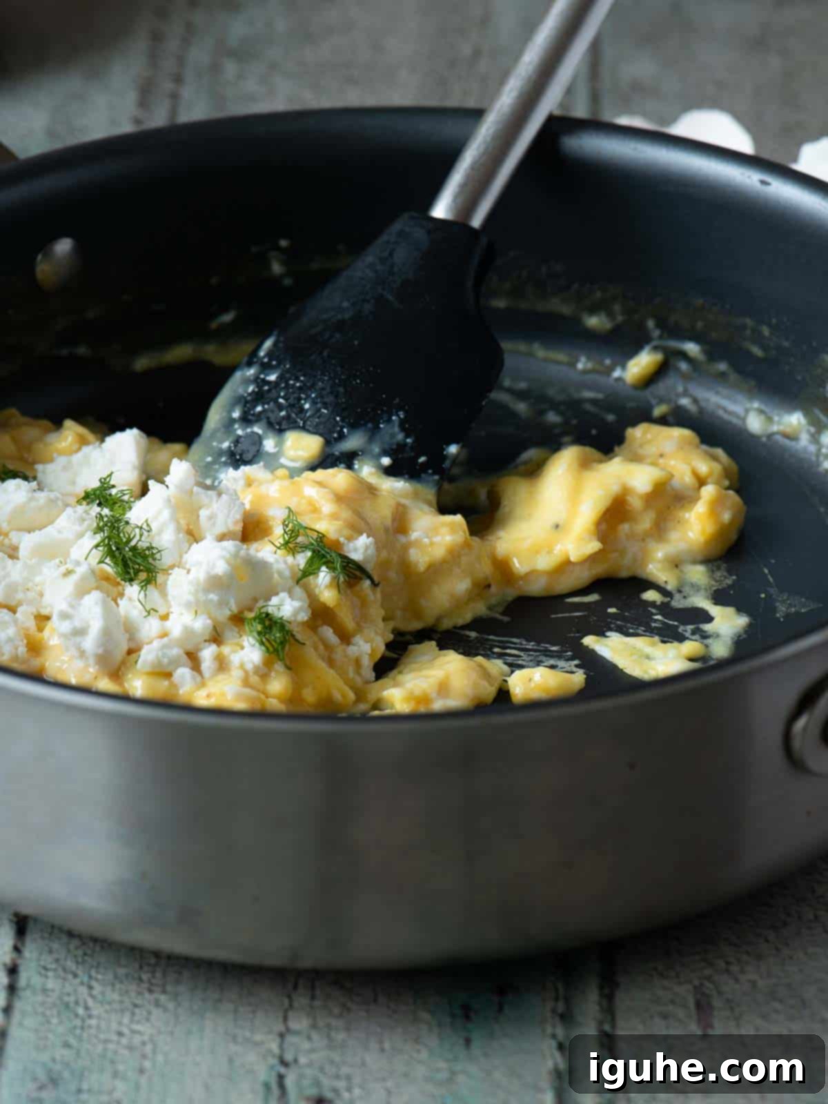 Mediterranean Feta Dill Scramble 7 Scrambled eggs being prepared in a skillet with a spatula and toppings.