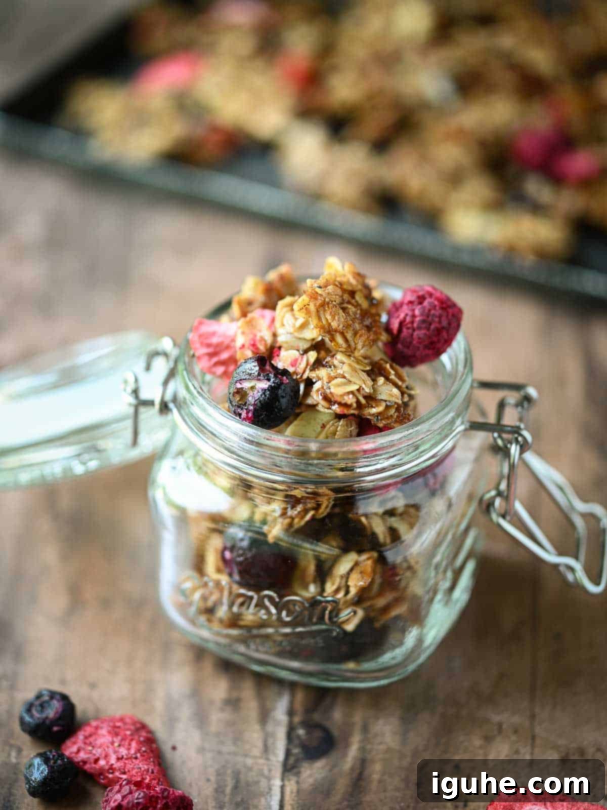 Berry granola in a clear mason jar on a wood surface.