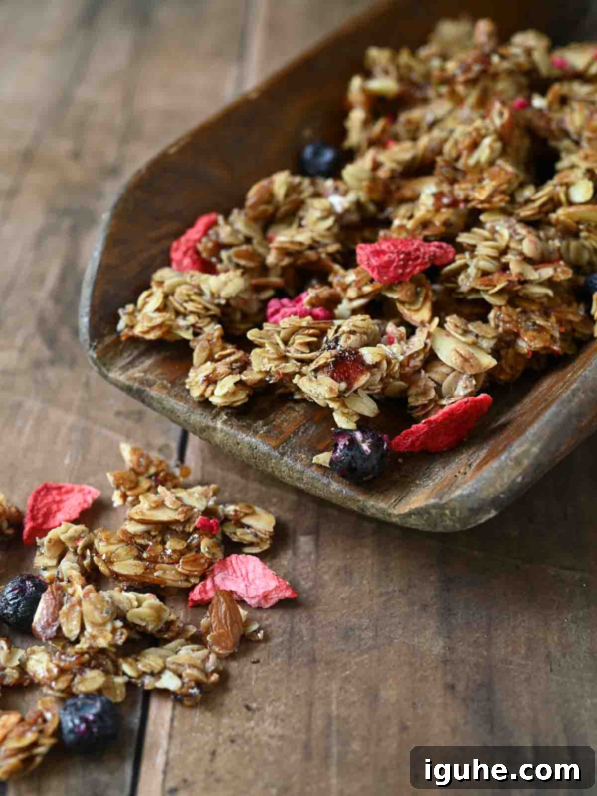 Berry Harvest Granola 8 Mixed berry granola falling off a large wooden scoop.