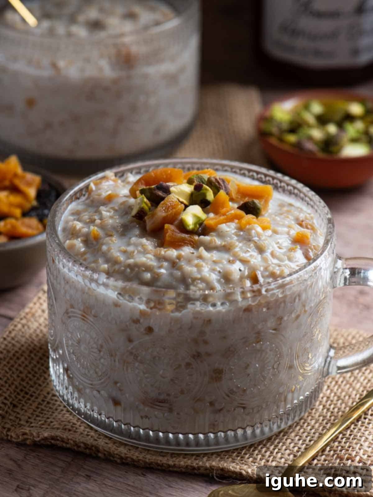 Velvet Apricot Porridge 9 Close-up of apricot oatmeal in a clear mug with pistachios and apricots in the back.