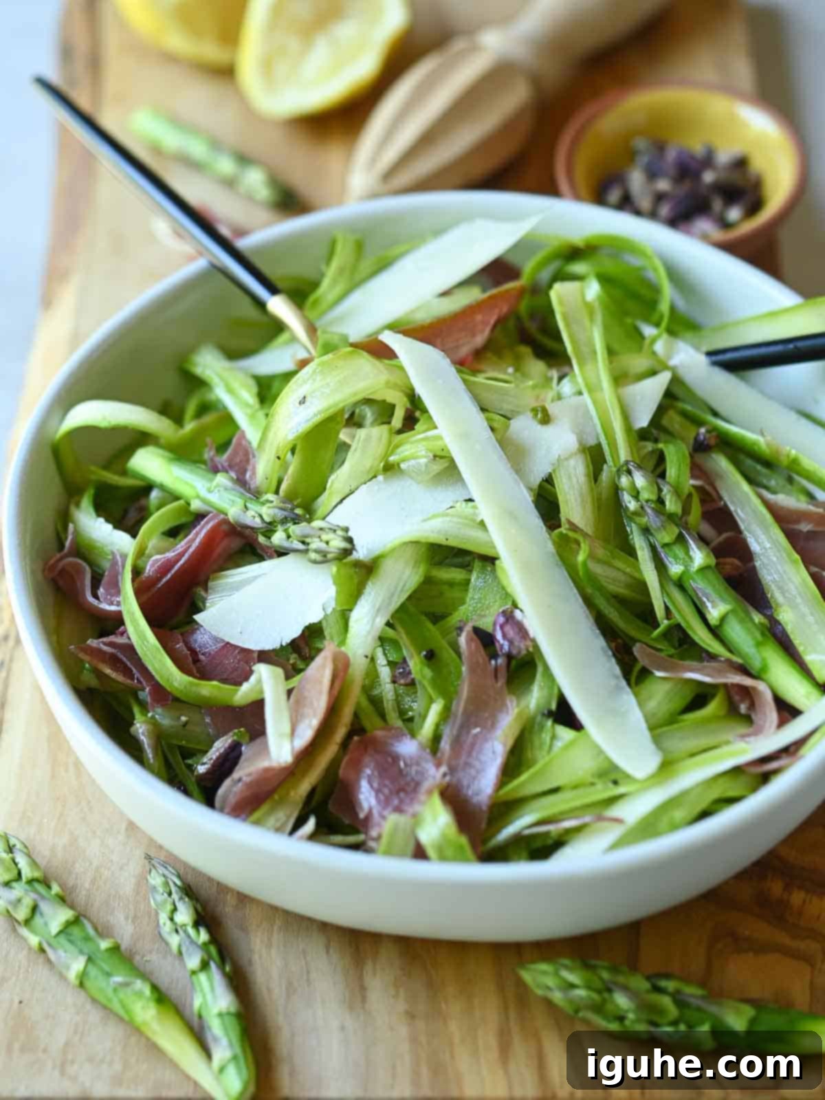 Delicate Asparagus & Prosciutto Salad 2 Angled view of shaved asparagus salad on a wood board with utensils in it.