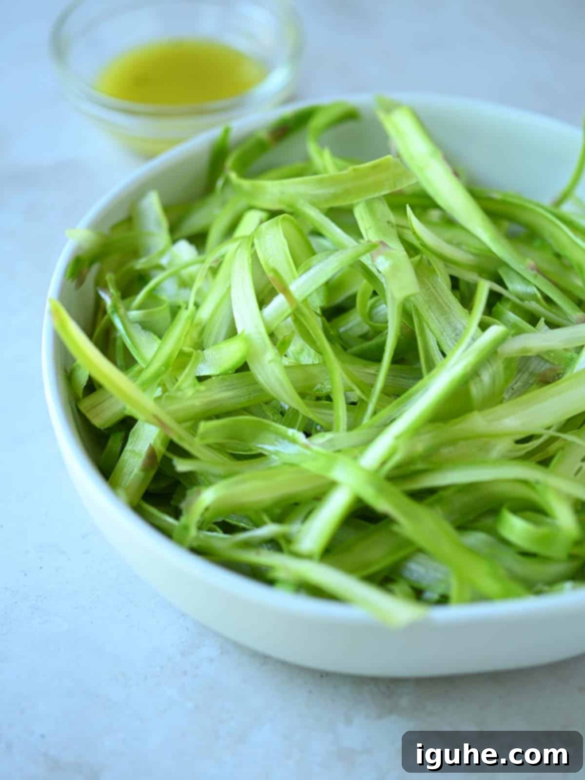 Delicate Asparagus & Prosciutto Salad 6 Raw shaved asparagus in a white bowl.