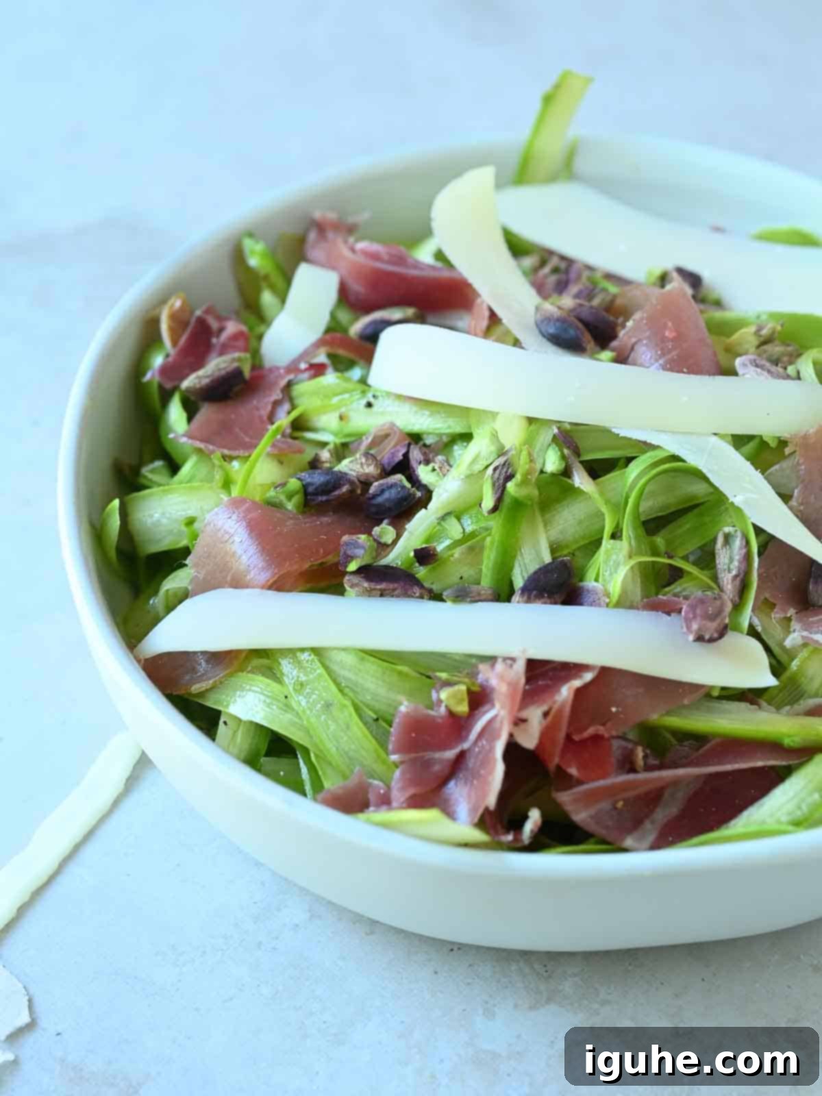 Delicate Asparagus & Prosciutto Salad 7 Asparagus salad in a white bowl with toppings.