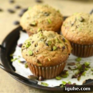 Decadent Pistachio Chocolate Chip Muffins 8 Three pistachio muffins on a black tray with scattered pistachios, looking inviting and delicious.