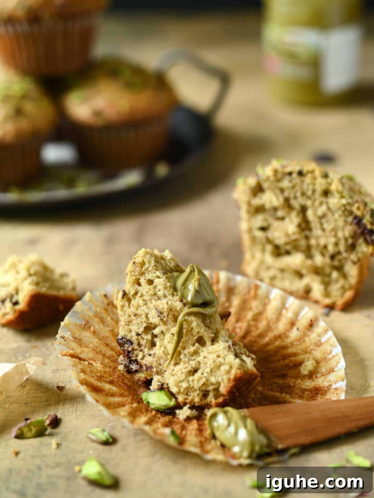 Decadent Pistachio Chocolate Chip Muffins 7 A perfectly halved pistachio muffin reveals its moist, tender interior, studded with vibrant green pistachios and melted chocolate chips, topped with a generous spread of creamy pistachio cream.