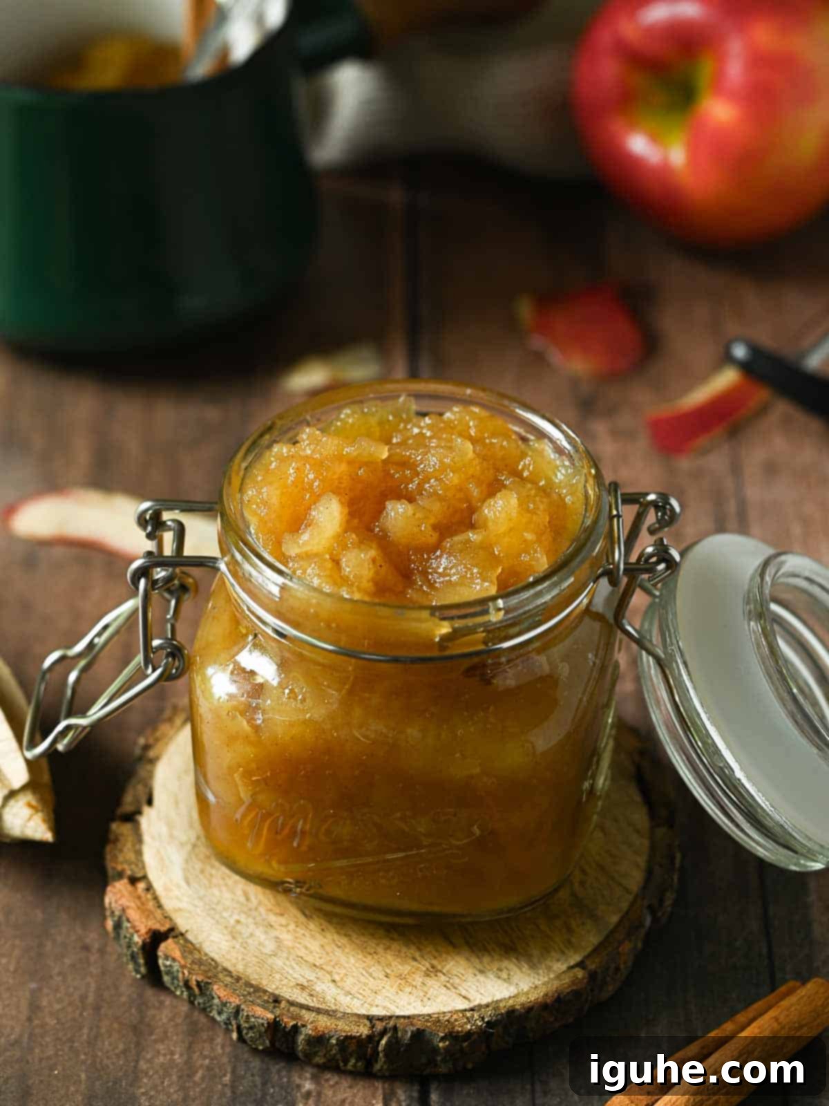 Spiced Honeycrisp Applesauce 2 Honeycrisp applesauce in a clear Mason Jar on a wood surface with an apple in the back.