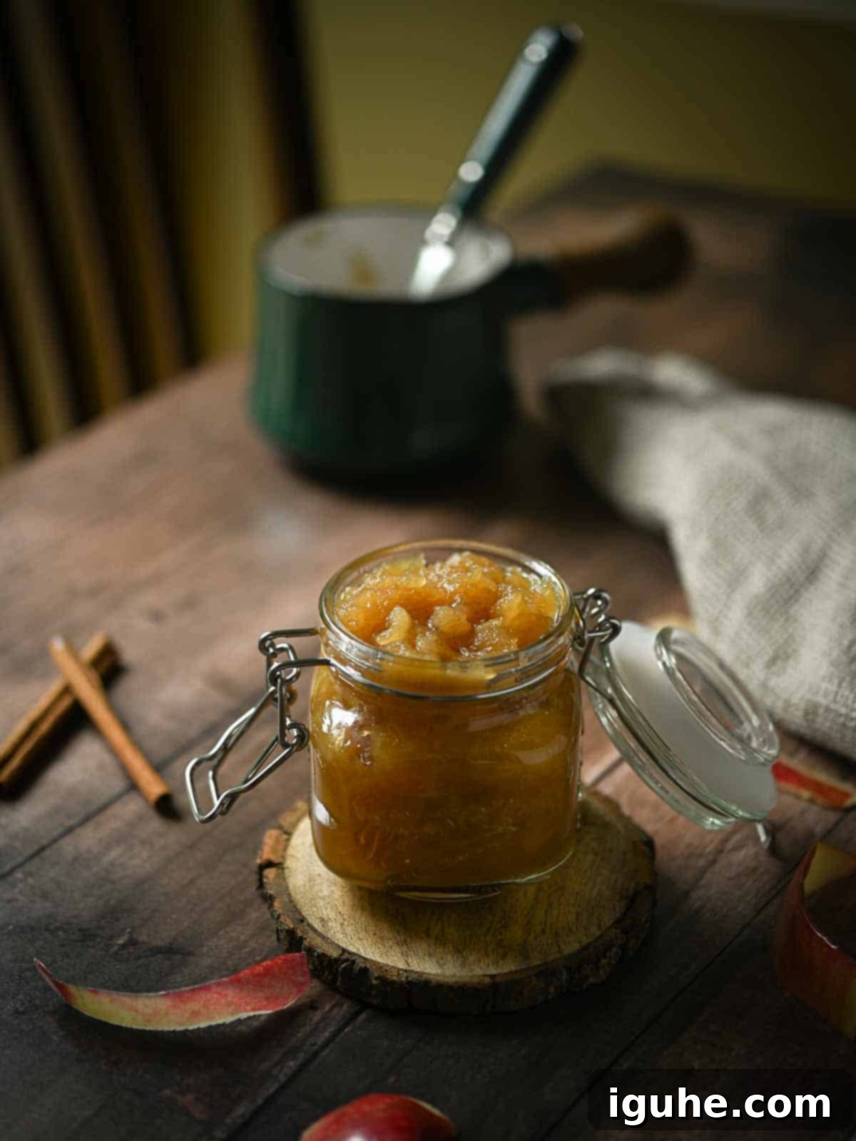 Spiced Honeycrisp Applesauce 3 A moody shot of Honeycrisp applesauce in a clear jar on a wooden table with a pot in the background.