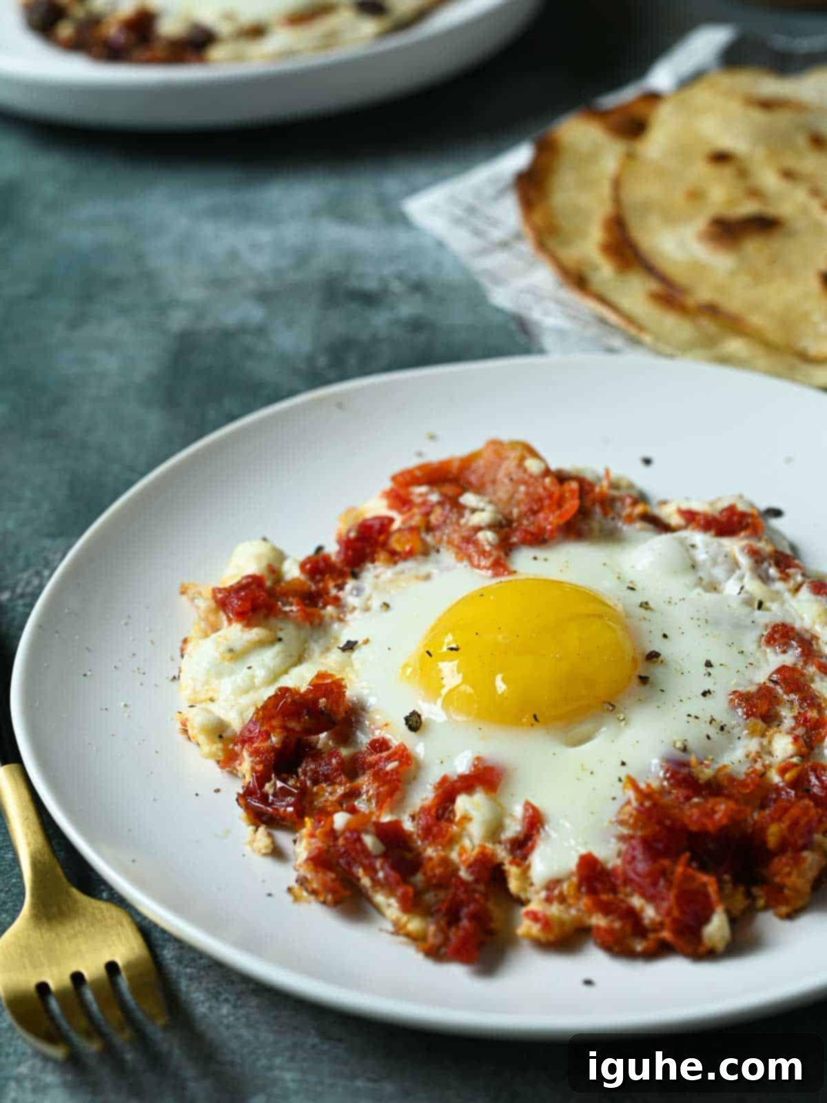 Perfectly cooked sun-dried tomato and feta fried egg on a white plate with a slice of toasted bread in the background, ready for a delicious breakfast.