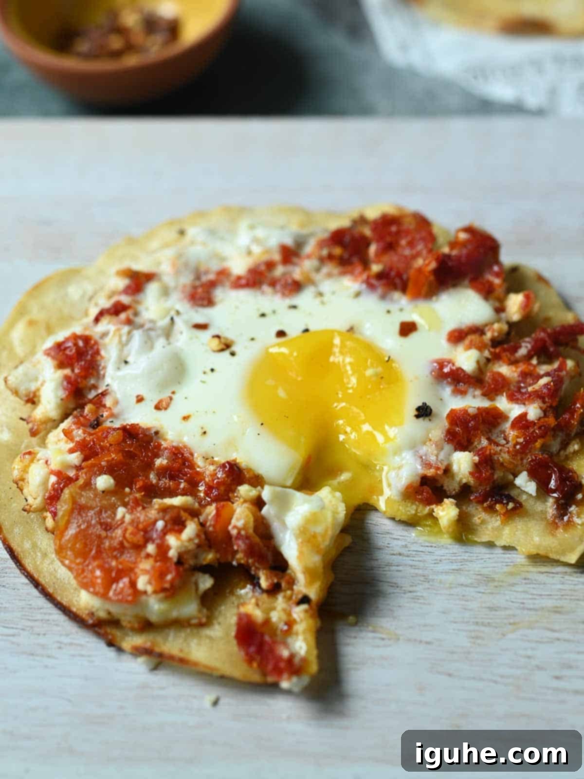 Sun-Kissed Feta and Tomato Fried Eggs 9 Sun-dried tomato and feta fried egg on a rustic wooden cutting board, with a visible piece of the golden, crispy feta crust.