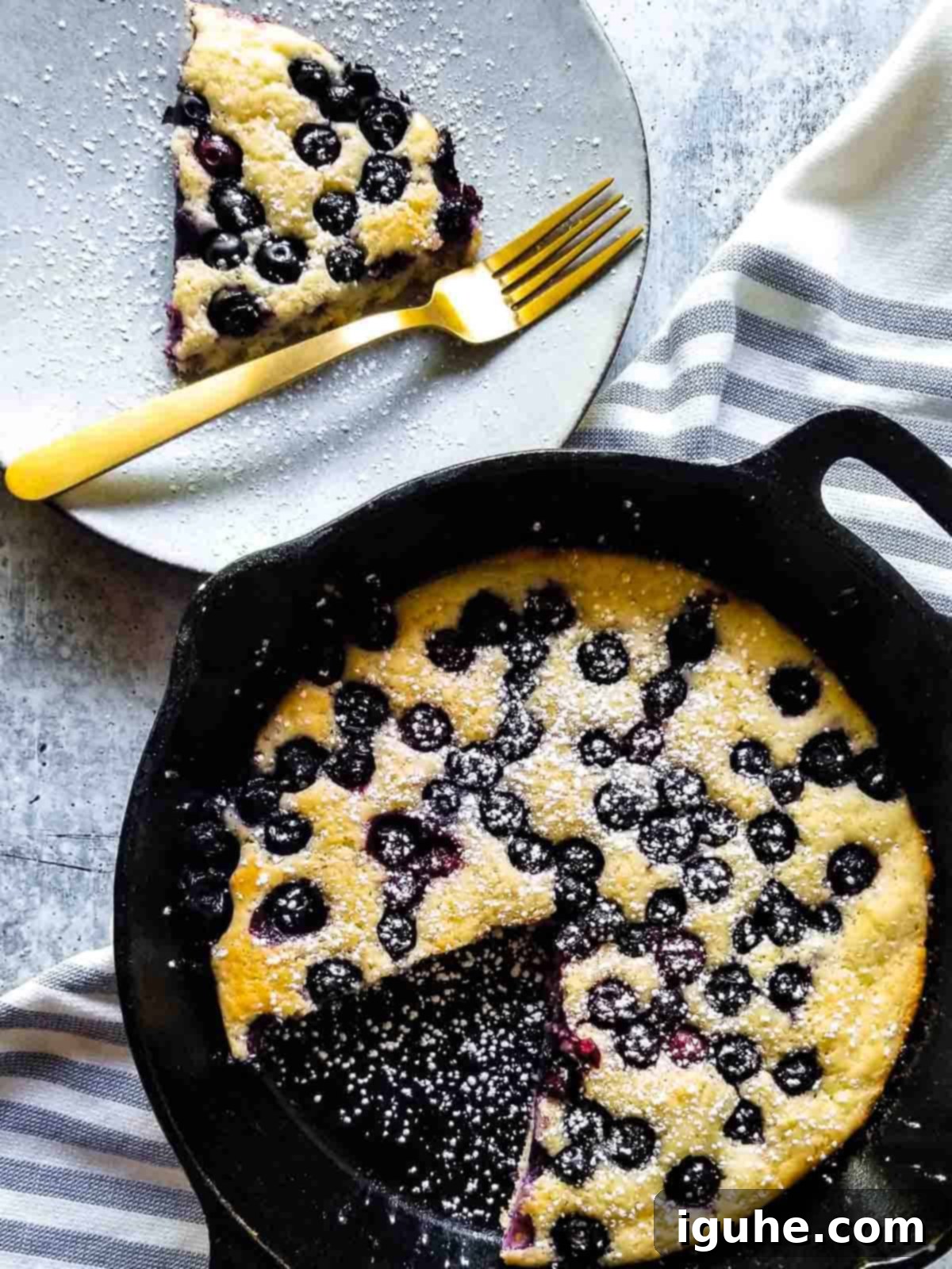 Blueberry Burst Skillet Pancake 2 Overhead view of blueberry pancake skillet with a slice cut out on a plate in a black skillet