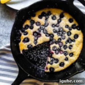 Blueberry Burst Skillet Pancake 12 Overhead view of blueberry pancake skillet with a slice cut out on a plate in a black skillet