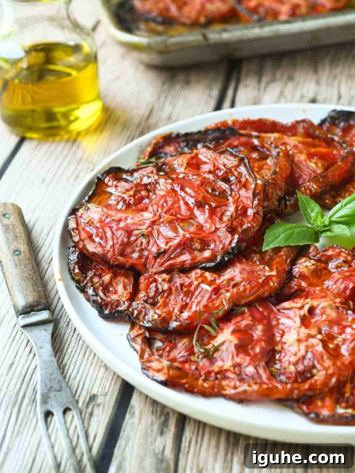 Roasted red tomatoes on a white plate with a fork next to it.