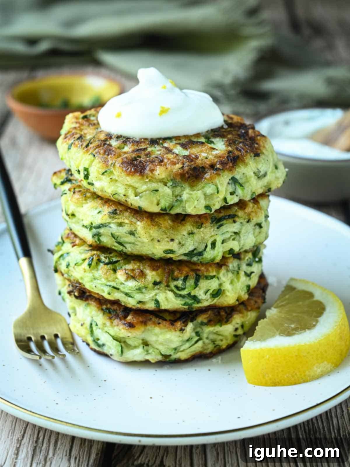 Stacked zucchini pancakes with a lemon slice to the side, garnished with fresh herbs and a sprinkle of sea salt.