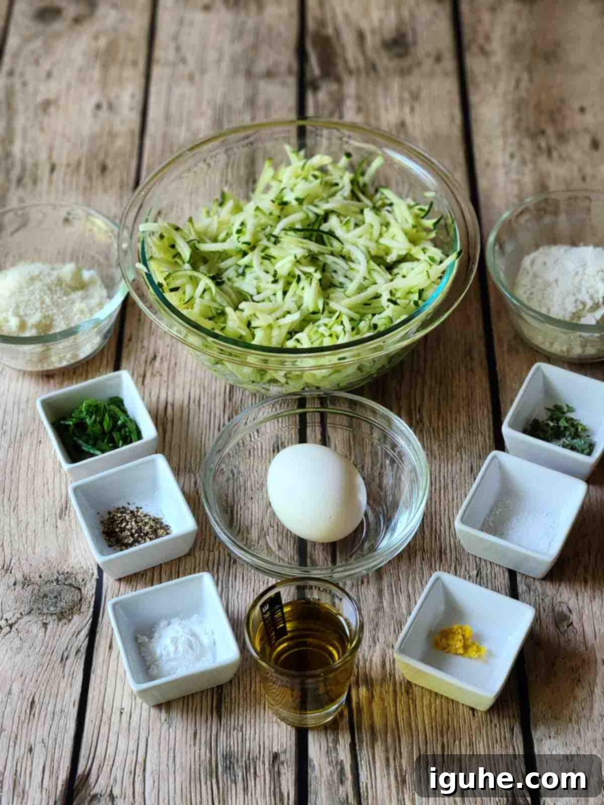 Crispy Zucchini Parmesan Fritters 3 A selection of fresh ingredients laid out on a wooden table, including zucchini, Parmesan cheese, eggs, flour, olive oil, and various fresh herbs.