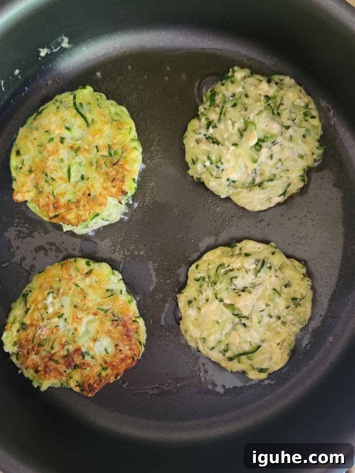 Crispy Zucchini Parmesan Fritters 6 Four zucchini pancakes sizzling in a hot skillet with olive oil, cooking to a golden brown.