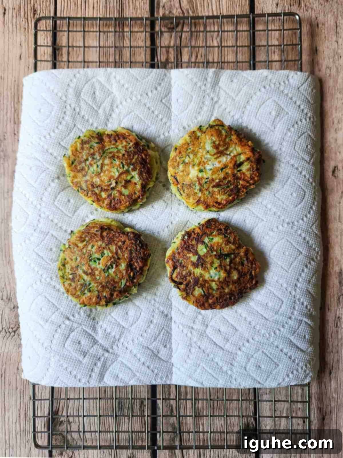 Crispy Zucchini Parmesan Fritters 7 Four freshly cooked, golden-brown zucchini pancakes resting on a wire rack, allowing excess oil to drain.