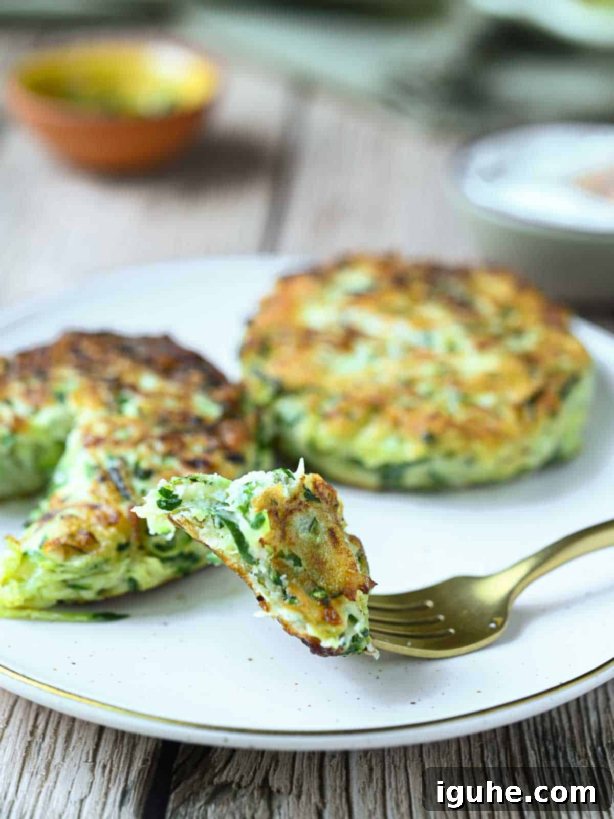 Crispy Zucchini Parmesan Fritters 9 Two parmesan zucchini fritters on a plate, one with a forkful taken out, showing the texture of the inside.