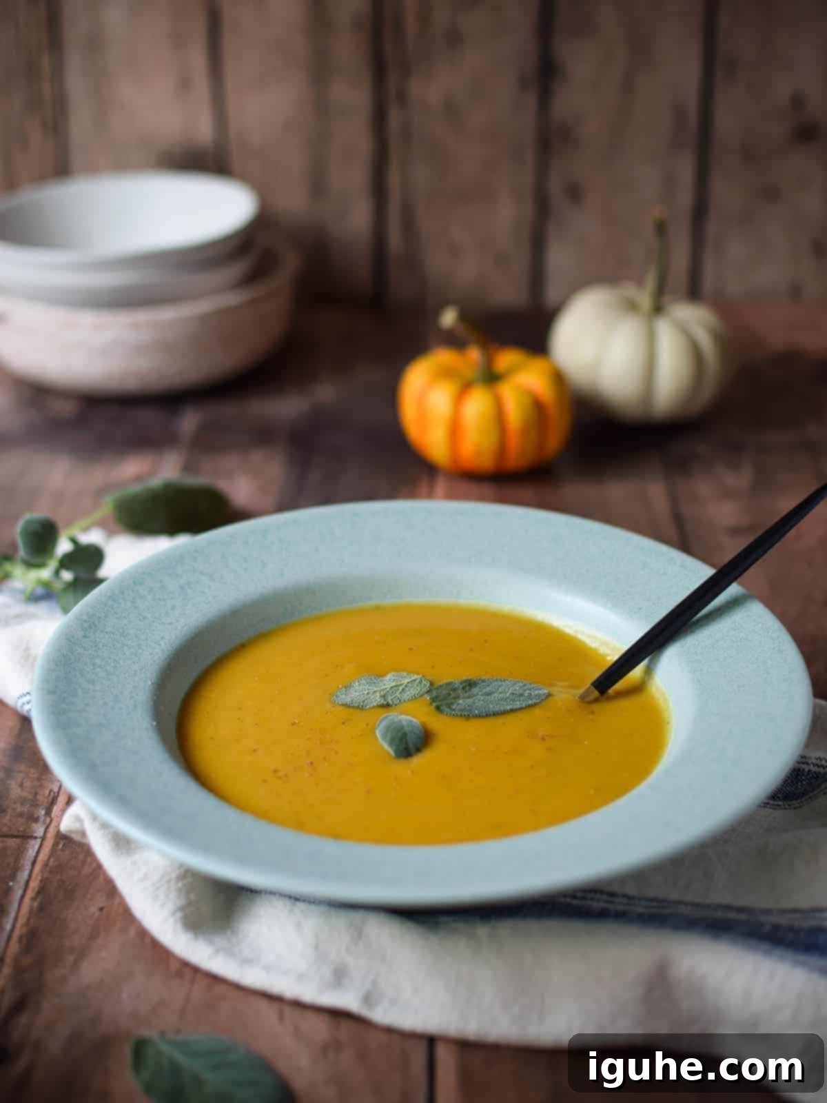 Golden Harvest Squash Soup 1 A comforting bowl of creamy autumn squash soup, garnished with fresh sage leaves, on a rustic wooden table with decorative pumpkins.