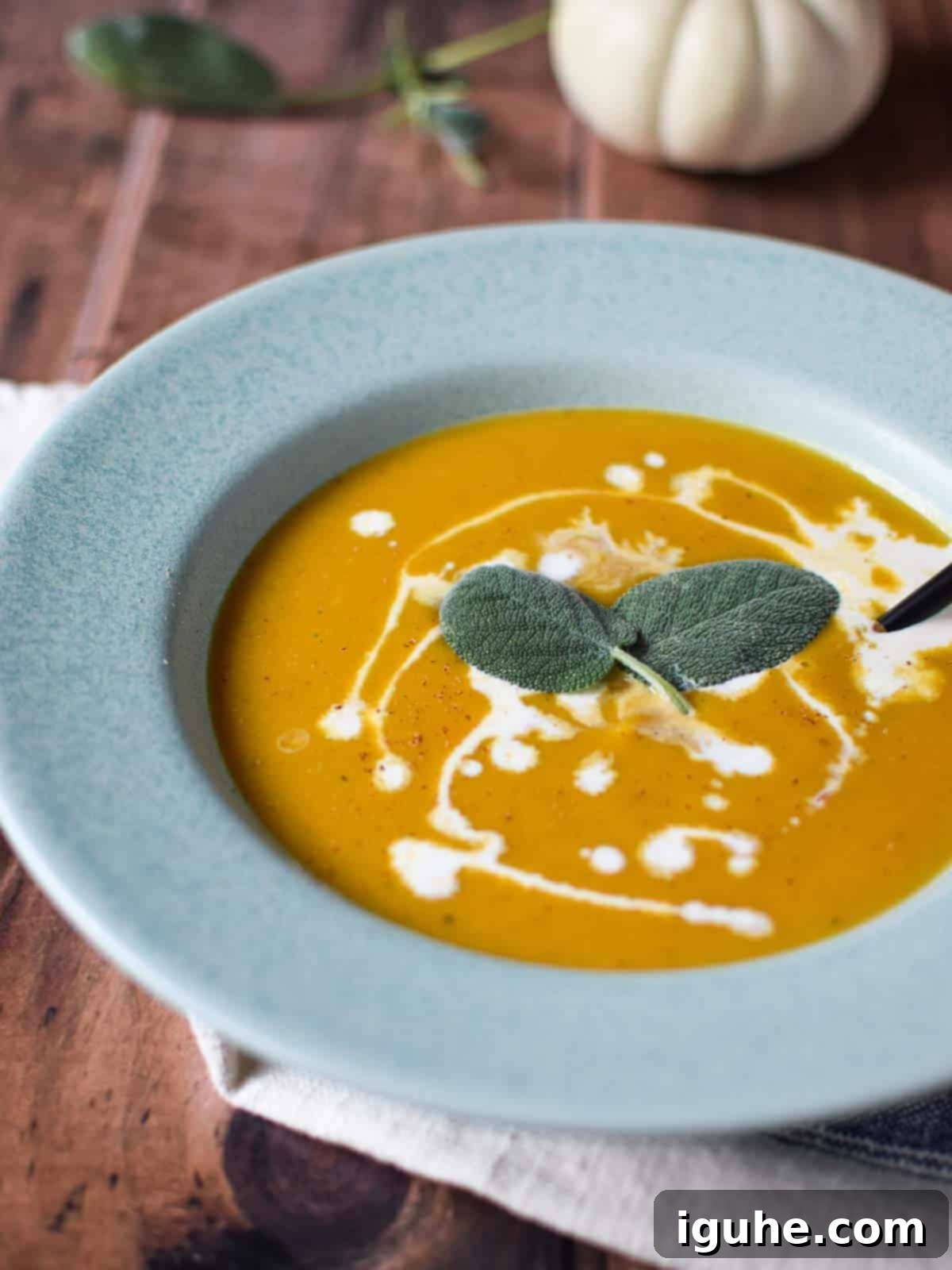 Golden Harvest Squash Soup 12 Close-up of creamy squash soup in a blue bowl with delicate drizzles of cream and a fresh sage leaf garnish.