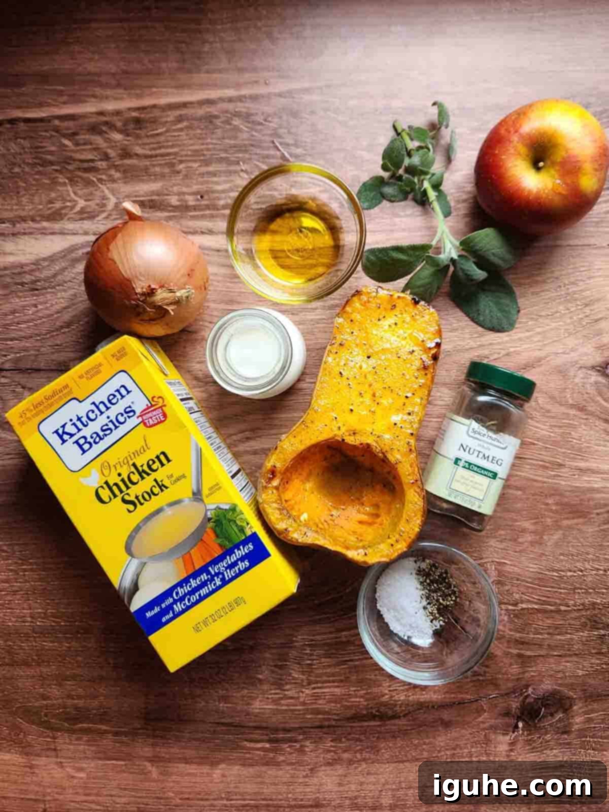 A collection of fresh ingredients for squash soup, including squash, apples, onions, and sage, arranged on a rustic wooden background.