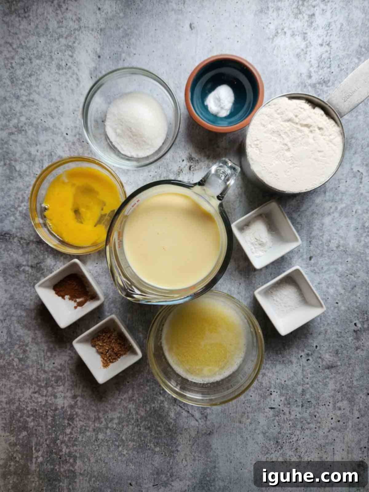 Festive Spiced Eggnog Waffles 3 All essential ingredients for making eggnog waffles neatly arranged on a white surface, including flour, spices, eggs, butter, and a carton of eggnog.