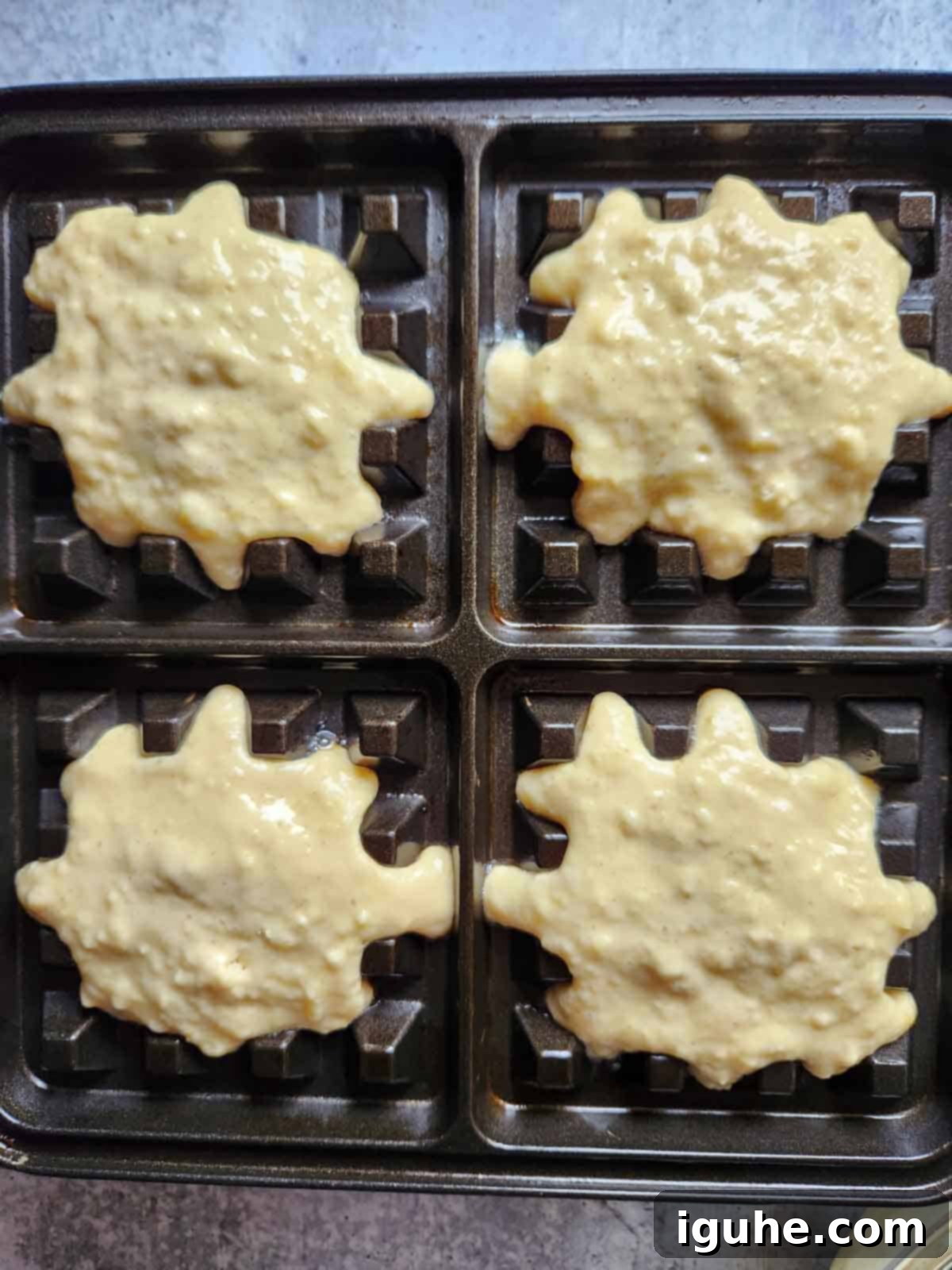 Festive Spiced Eggnog Waffles 8 Thick eggnog waffle batter being carefully poured onto the hot plates of a waffle iron, filling the sections evenly.