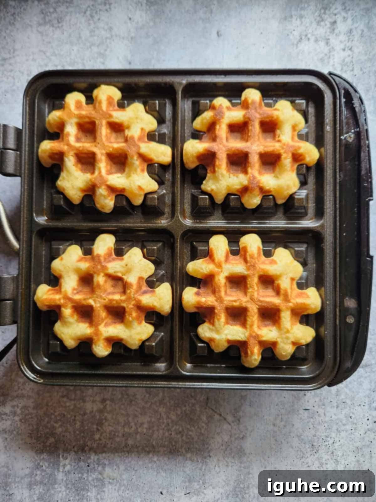 Festive Spiced Eggnog Waffles 9 Four perfectly cooked, golden-brown eggnog waffles sitting on the open waffle maker, ready to be removed and served.