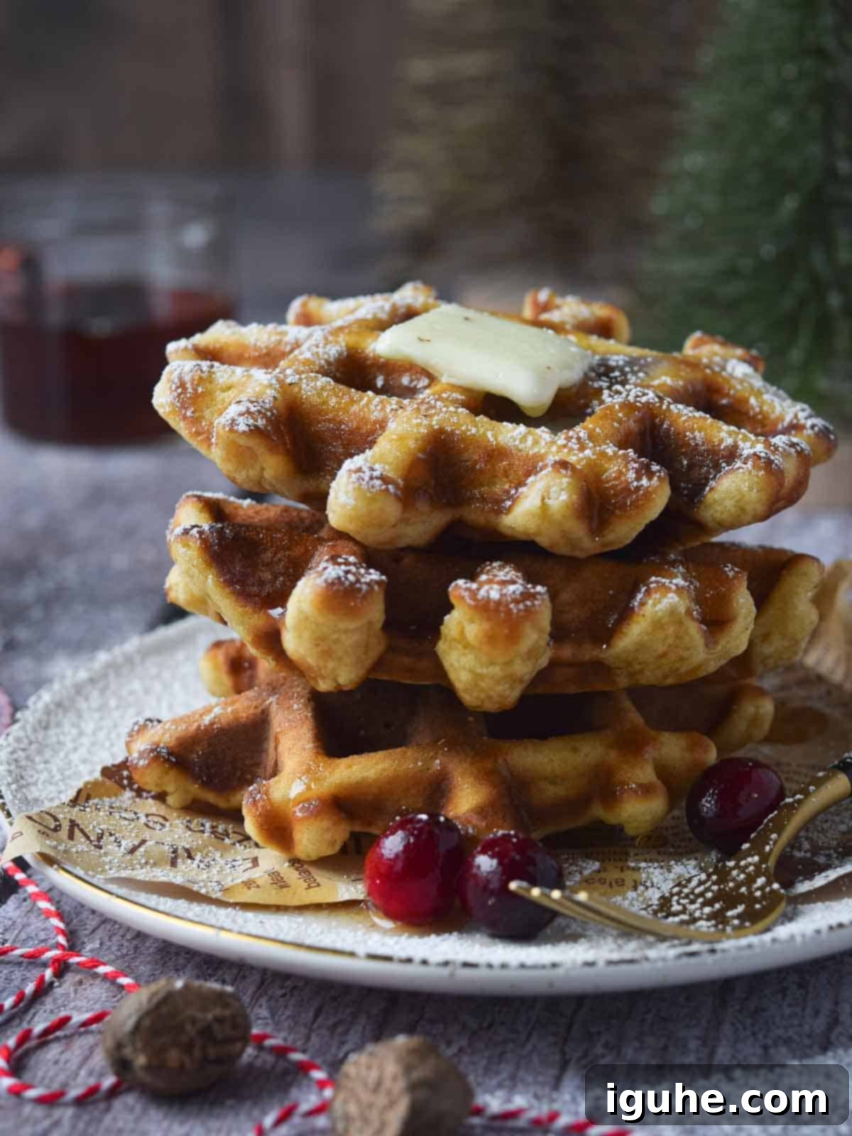 Festive Spiced Eggnog Waffles 10 A stack of golden eggnog waffles on a plate, adorned with a pat of butter and a generous dusting of powdered sugar, ready for enjoyment.