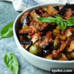 Vibrant Sicilian Eggplant Caponata 10 Close-up of eggplant caponata in a white bowl with basil leaves on top.