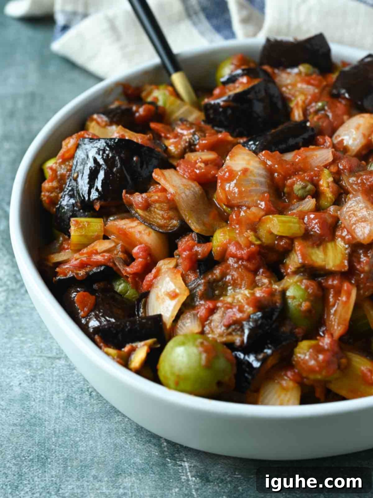 Vibrant Sicilian Eggplant Caponata 8 Eggplant caponata in a white bowl on a blue surface.