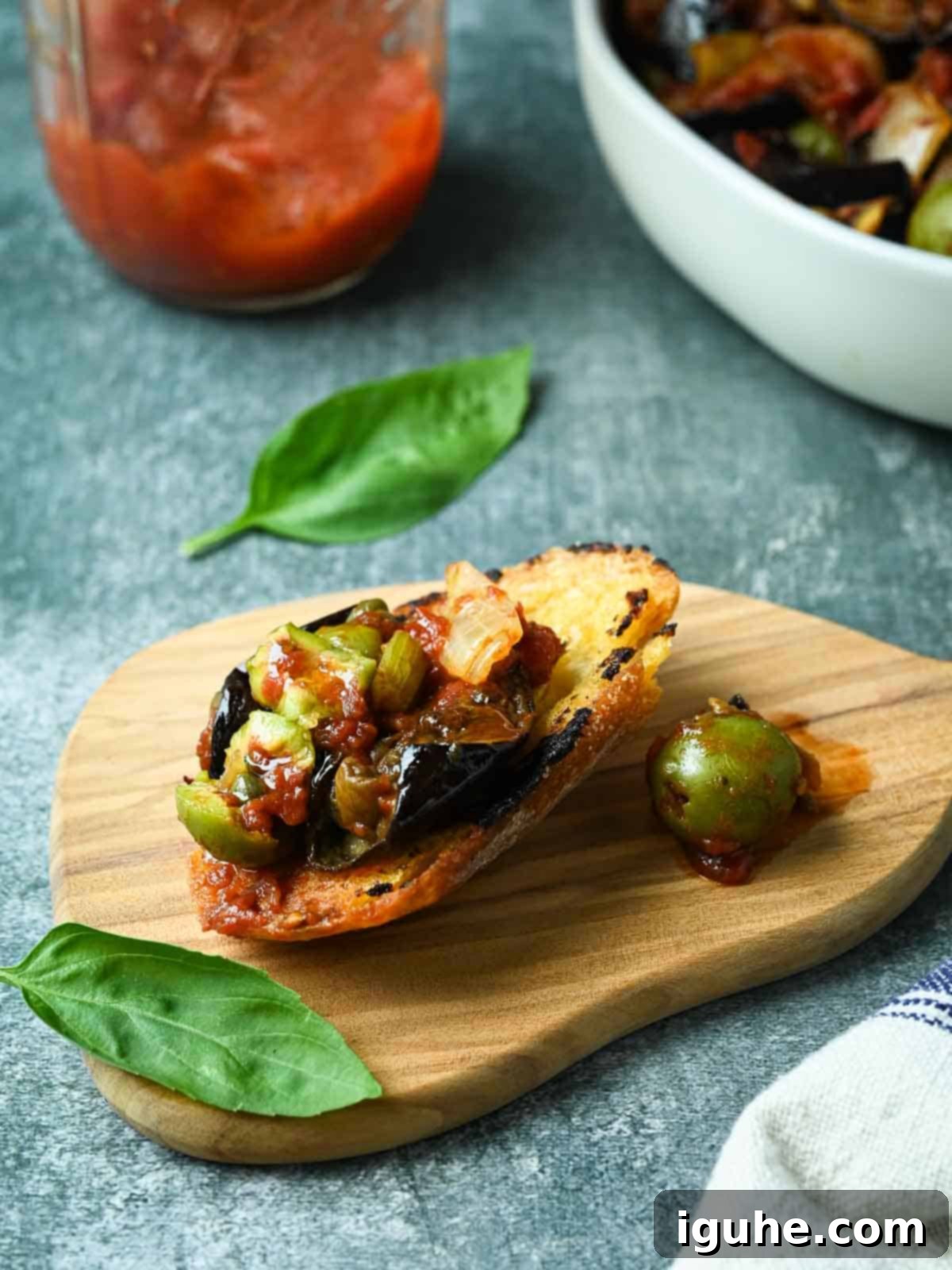 Vibrant Sicilian Eggplant Caponata 9 Piece of bread with caponata spread on it with basil and sauce on the side.