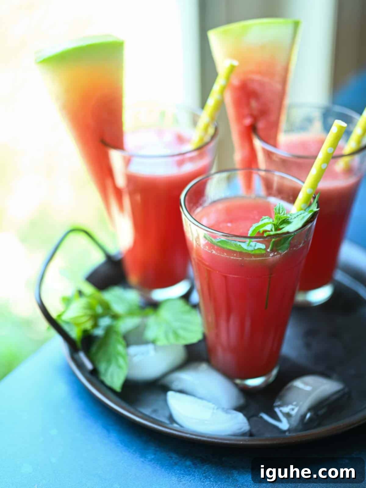 Three glasses of fresh watermelon water on a tray by the window, garnished with mint.