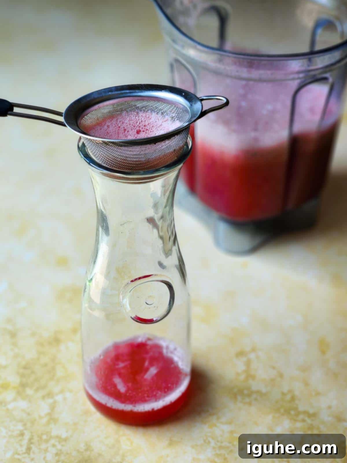 Pure Watermelon Refreshment 5 Blended watermelon juice in a glass pitcher with a fine-mesh strainer positioned on top, ready for straining.