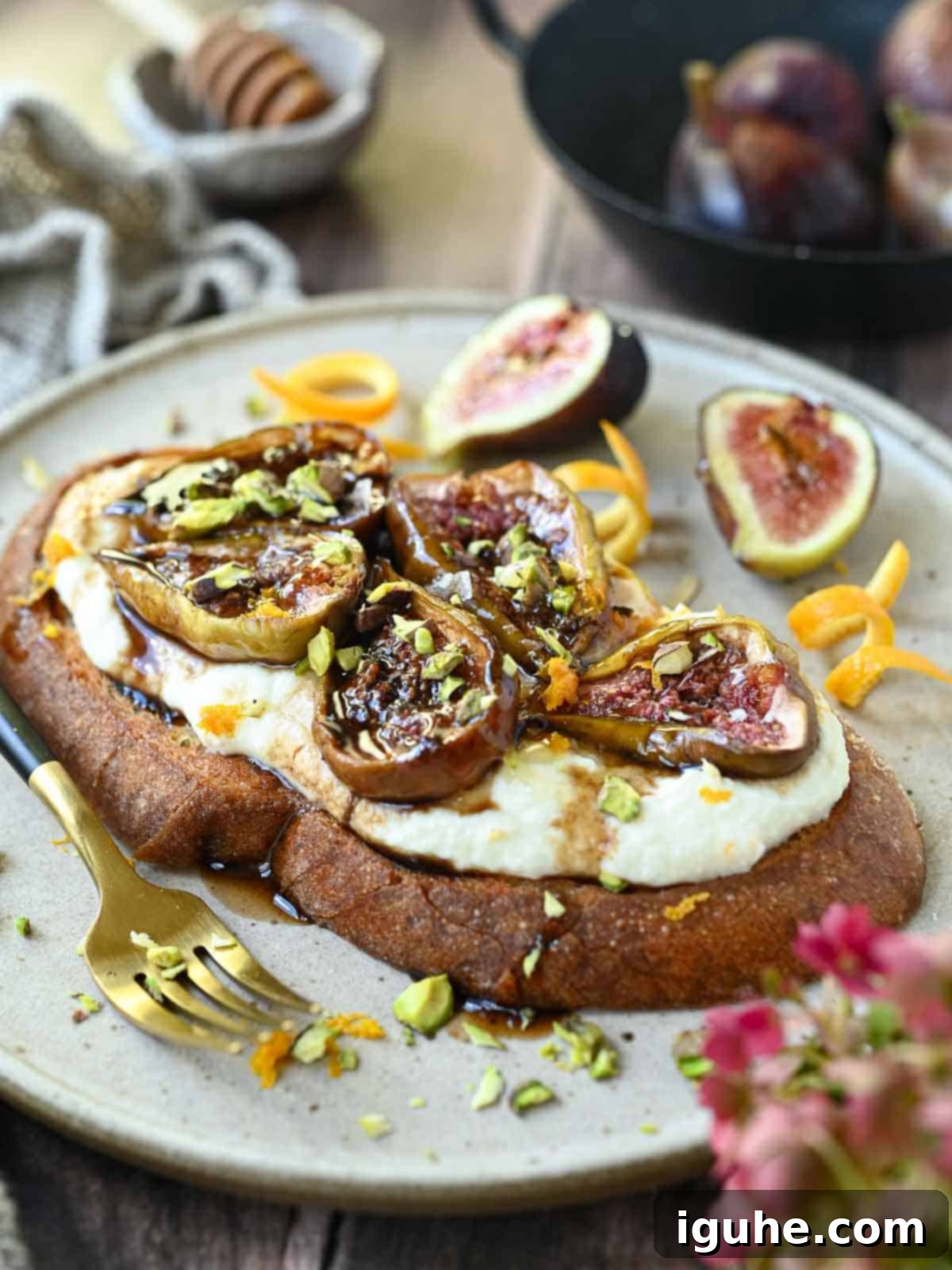 Gourmet fig toast on a beige plate, garnished with fresh figs, pistachios, and orange zest, with more fresh figs in the background.
