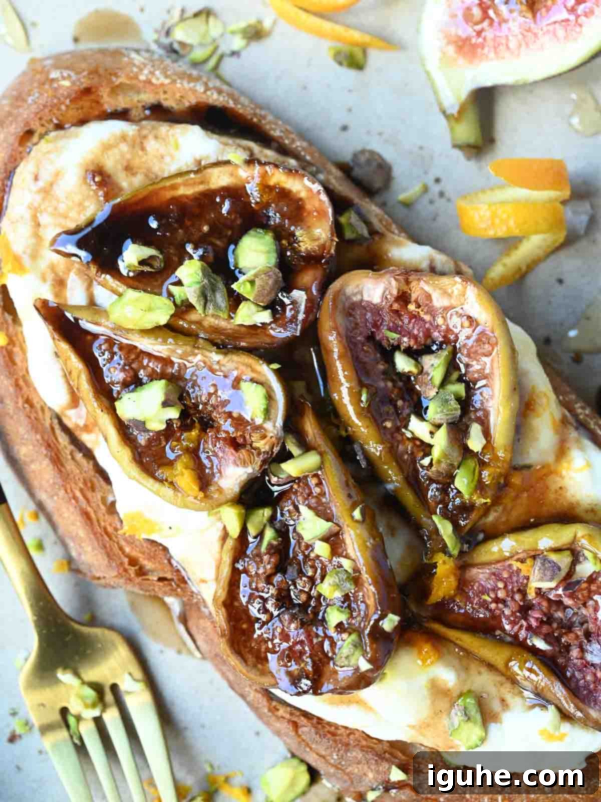 Sweet and Savory Balsamic Fig Toast 8 Overhead view of two slices of roasted balsamic fig toast, garnished with crushed pistachios and fresh orange zest, on a rustic plate.