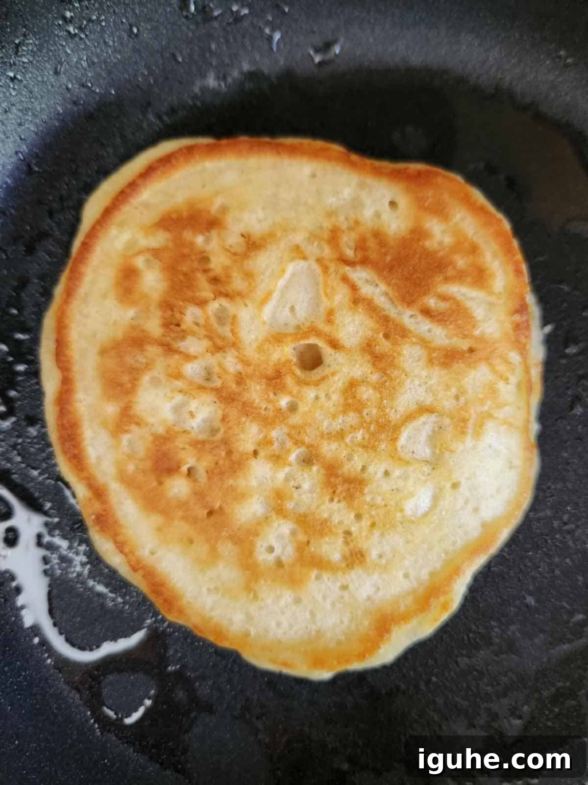 Decadent Brown Sugar Stacks 7 A brown sugar pancake cooking on a griddle, showing bubbles forming on the surface, indicating it's ready to flip.