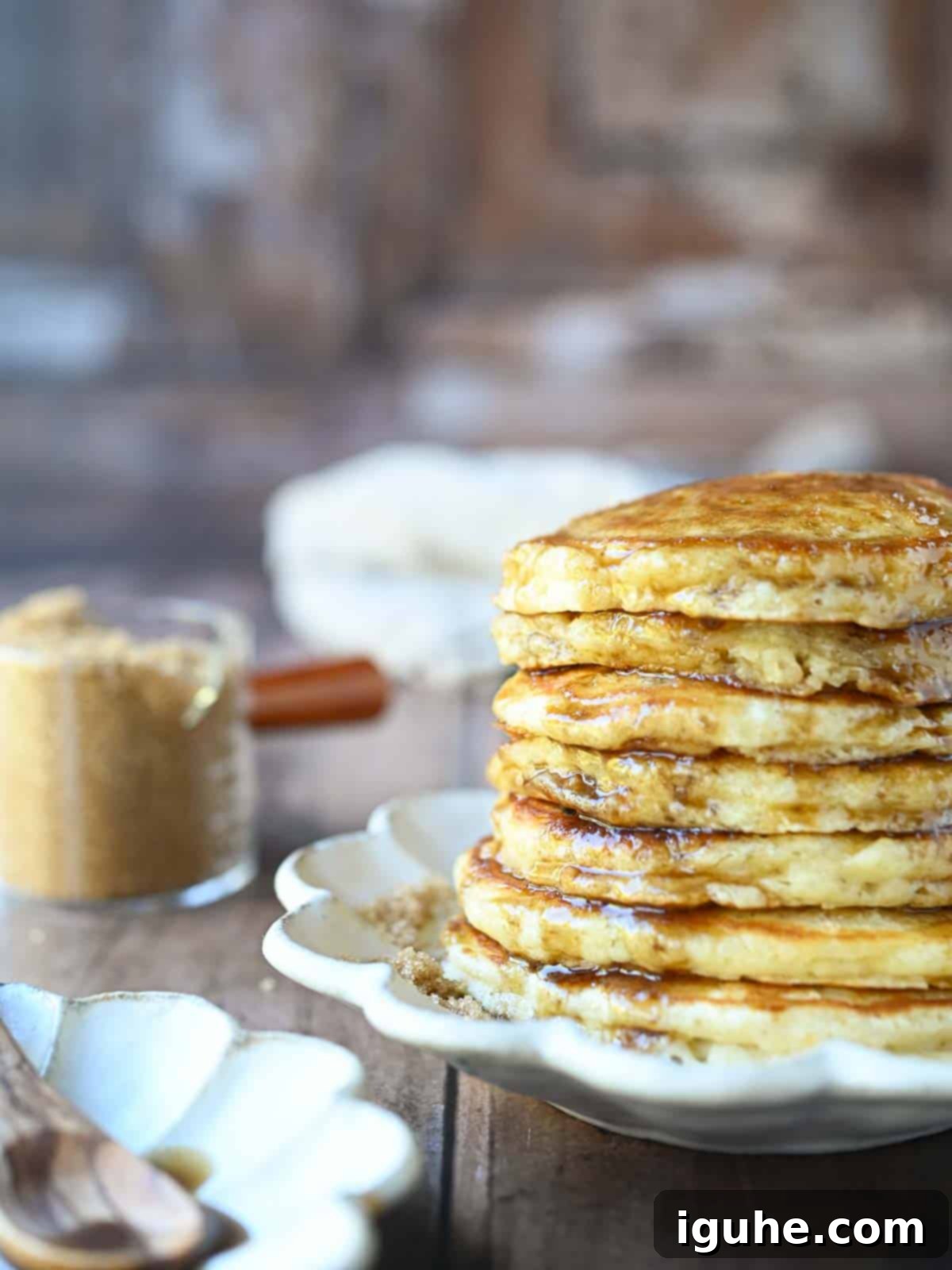 Decadent Brown Sugar Stacks 9 Eye-level view of a stack of fluffy brown sugar pancakes on a white plate, with a fork, ready to be eaten.