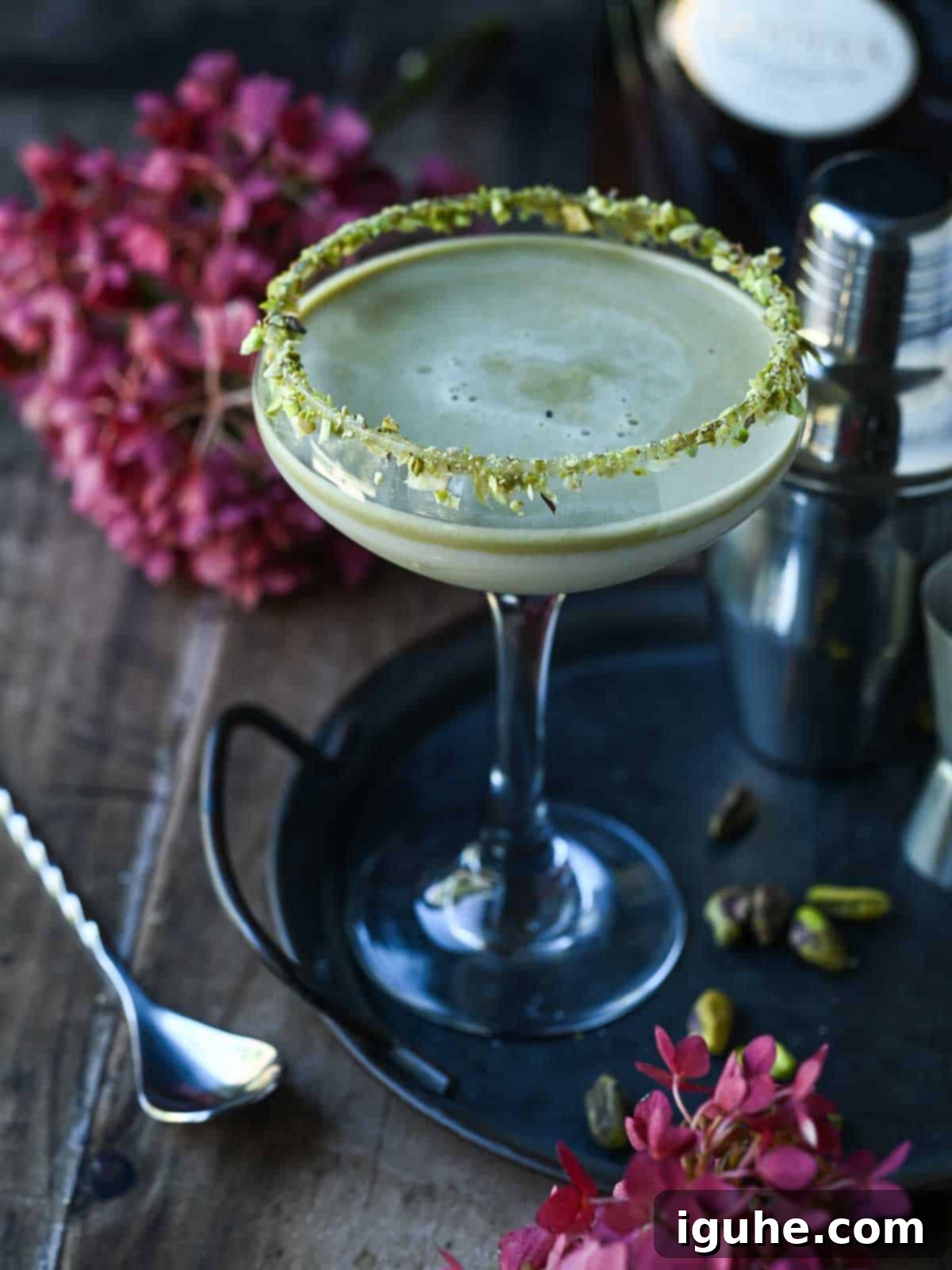 Pistachio martini on a tray with pink flowers next to it.