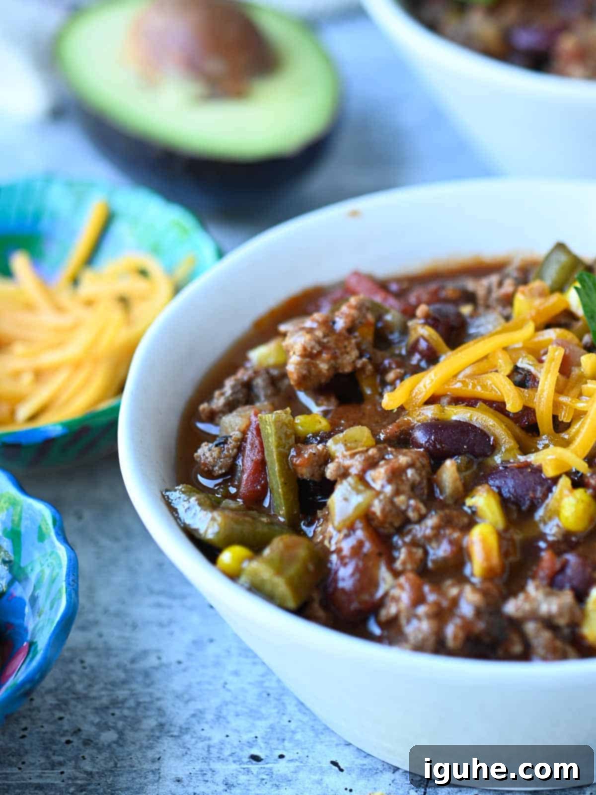 Fire Roasted Turkey Chili 3 Close-up of chili in a white bowl, with an avocado half and spoon in the background.