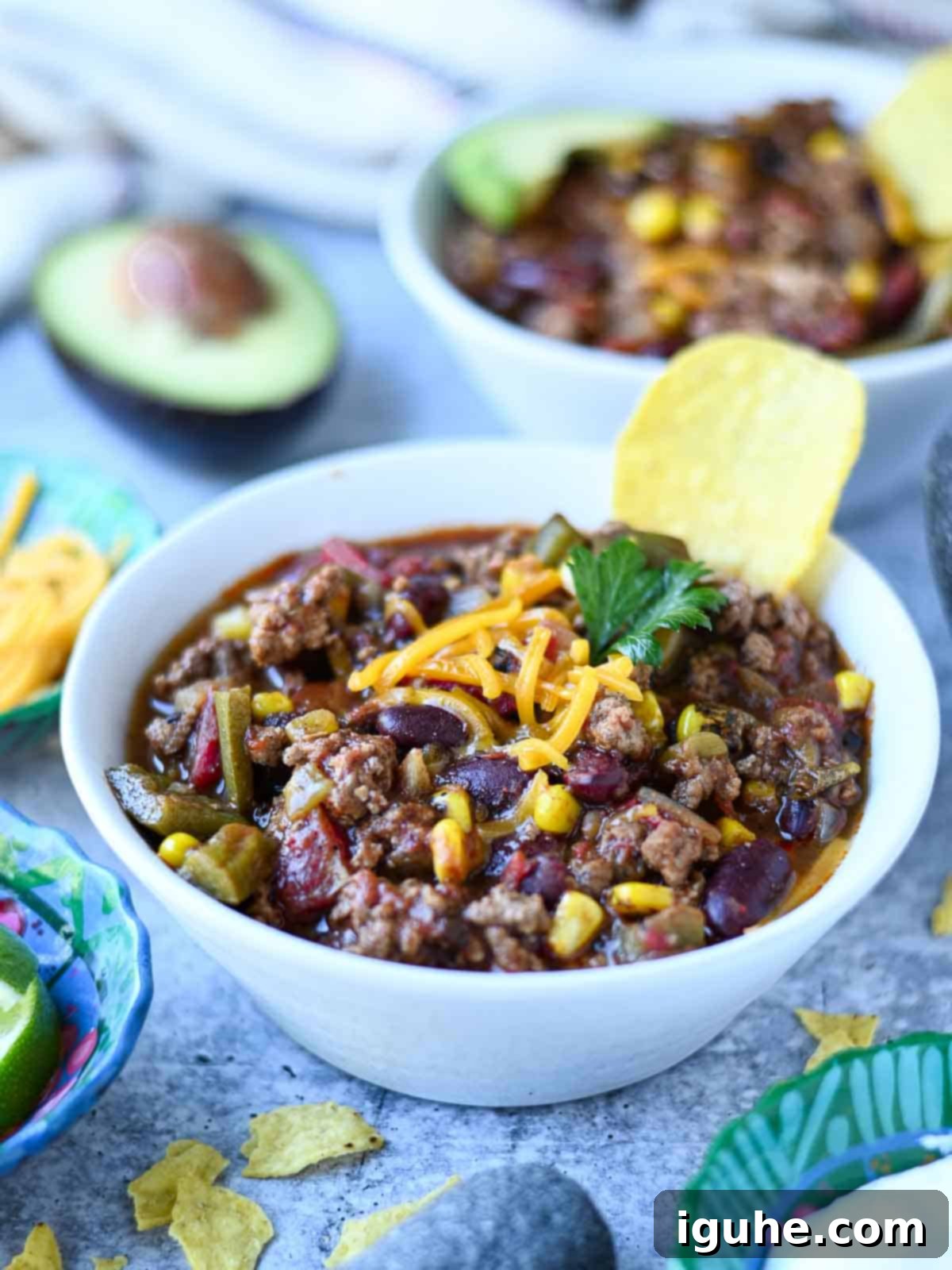 Fire Roasted Turkey Chili 8 Two bowls of chili in a white bowl on a blue surface, one garnished with cheese and sour cream.