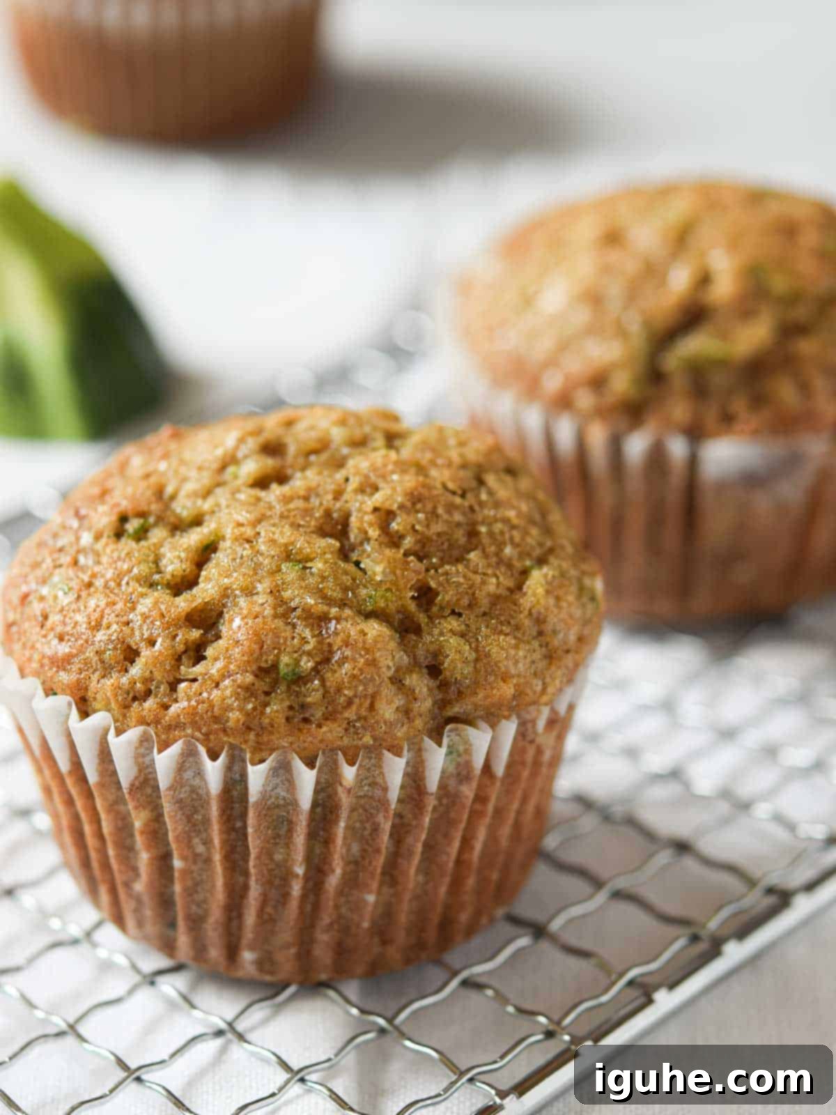 Zucchini muffins on a silver rack over a white surface.