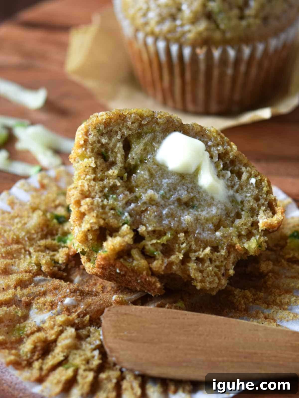 Apple-Kissed Zucchini Muffins 10 Muffins cut open with melted butter dripping on in on a wood surface.