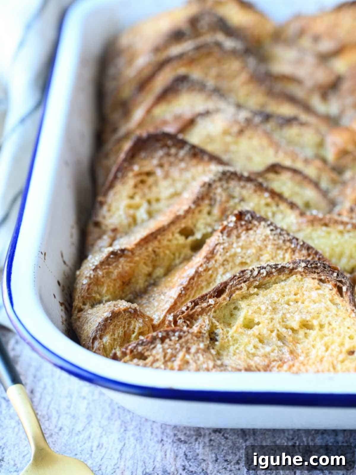 Baked French toast in a white enameled pan, topped with powdered sugar and berries.
