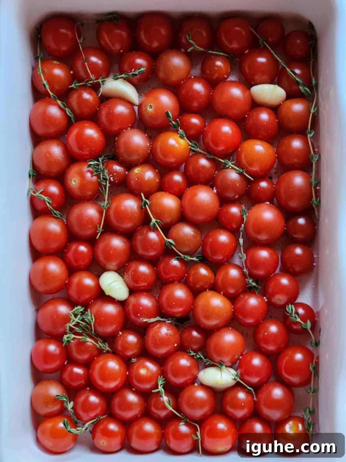 Cherry Tomato Confit with Garlic and Thyme 4 Tomatoes with garlic and thyme in a white baking pan.