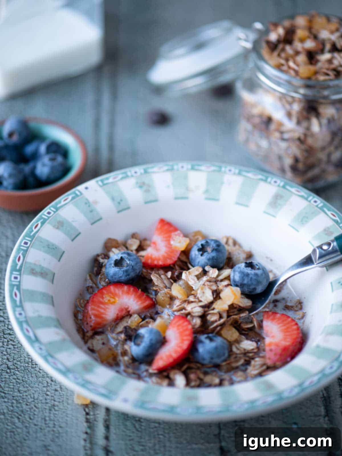Candied Orange Chocolate Muesli 8 A bowl of chocolate muesli with a spoon, fresh berries, and milk, ready for breakfast.