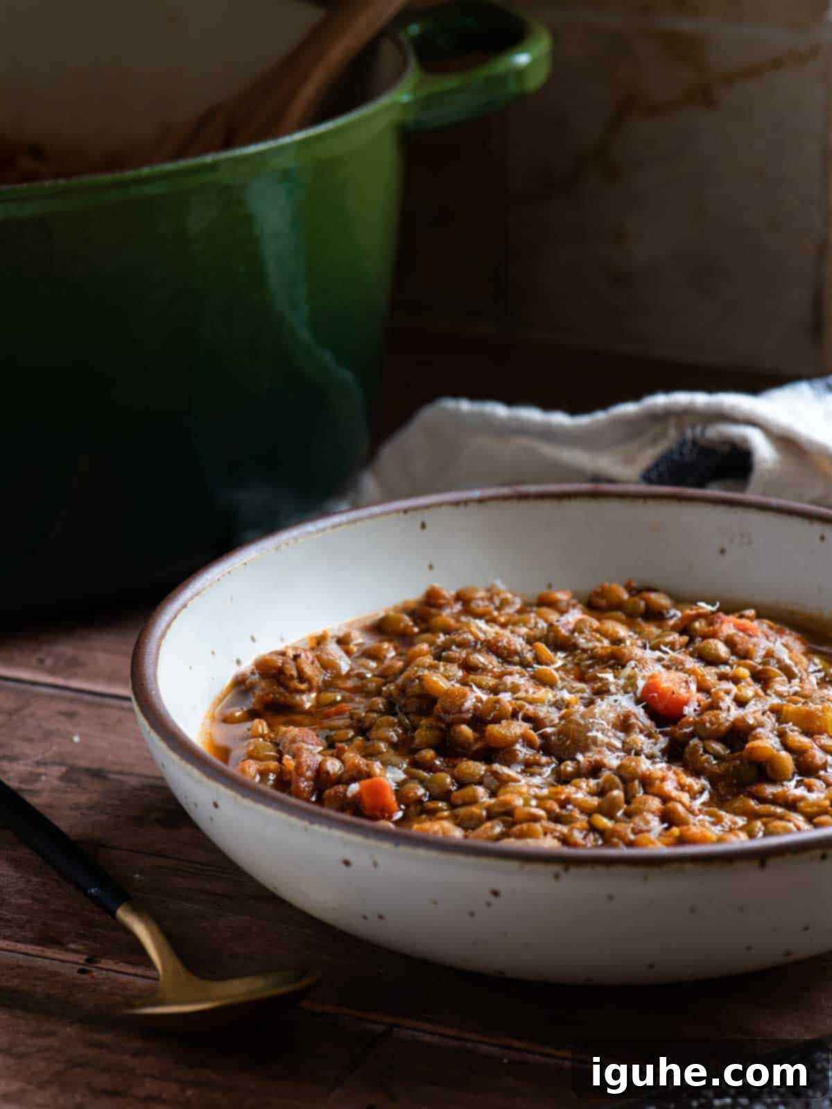 A steaming bowl of hearty bacon lentil soup, garnished with crispy bacon and fresh herbs, with a rustic green pot in the background, signaling warmth and home-cooked goodness.