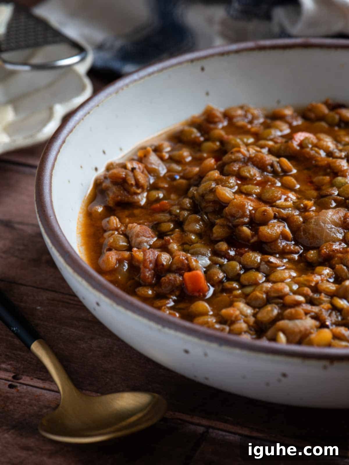 Hearty Bacon Lentil Soup 11 A rustic bowl of bacon lentil soup on a wooden surface with a spoon, ready to be enjoyed, highlighting its comforting and nourishing qualities.