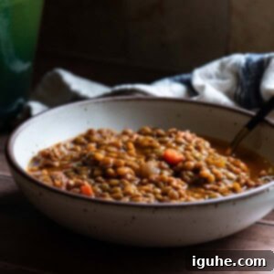 Hearty Bacon Lentil Soup 12 A beige bowl filled with hearty bacon lentil soup, a spoon resting inside, indicating a warm and inviting meal.