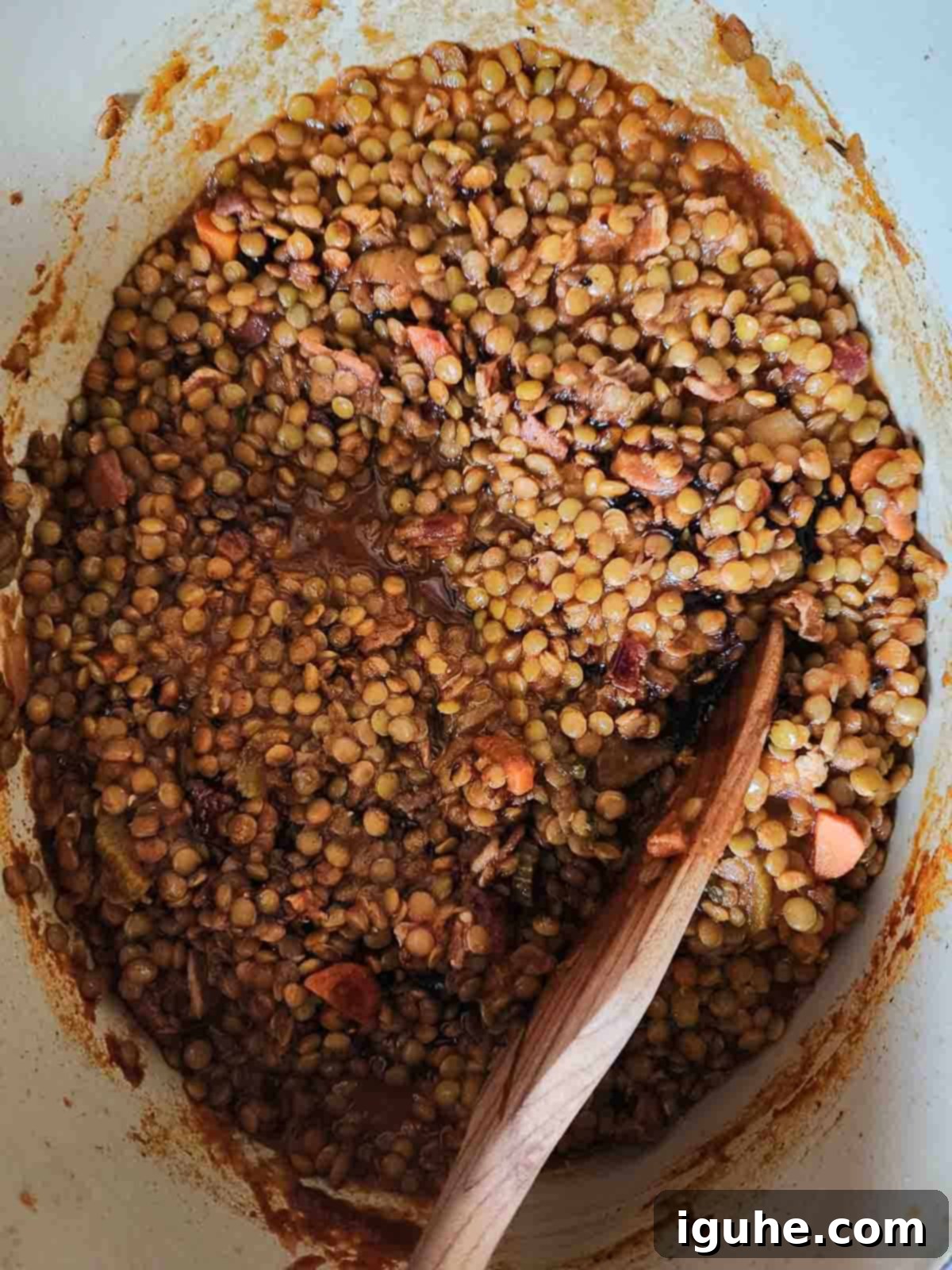 Hearty Bacon Lentil Soup 8 Hearty bacon lentil soup simmering gently in a pot with a wooden spoon, indicating the cooking process and development of rich flavors.