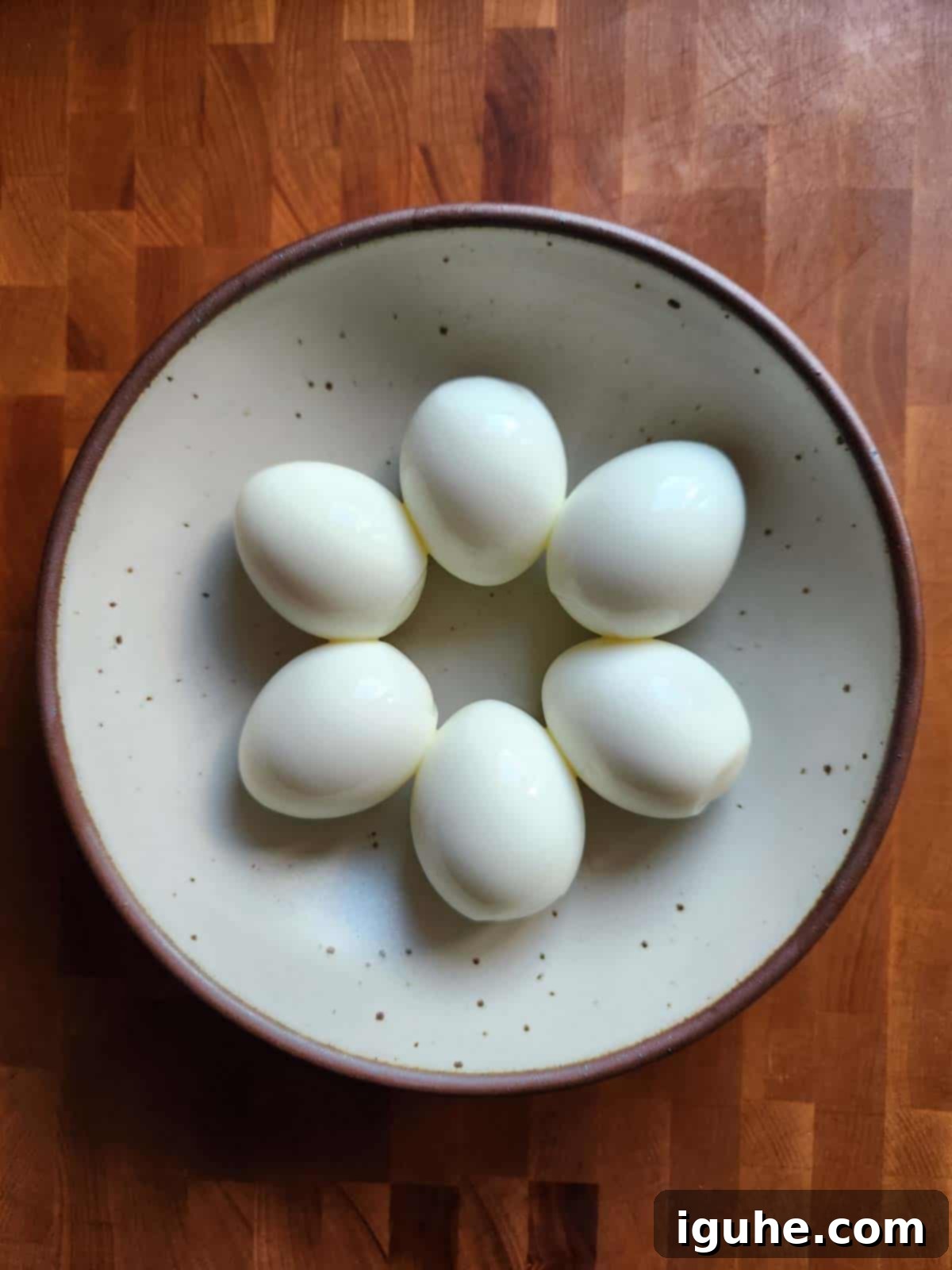 Umami Deviled Eggs 4 Overhead of six peeled hard-boiled eggs in a bowl.